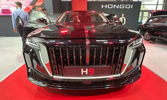 Elegancki czarny Hongqi H9 z chromowanym grillem i czerwonymi akcentami. Zainteresowani sprawdzają jego cenę na wystawie.