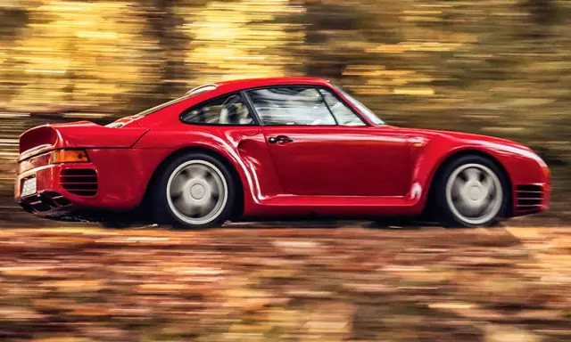 Czerwony Porsche 959 pędzi przez jesienny las, liście tworzą rozmyte smugi.