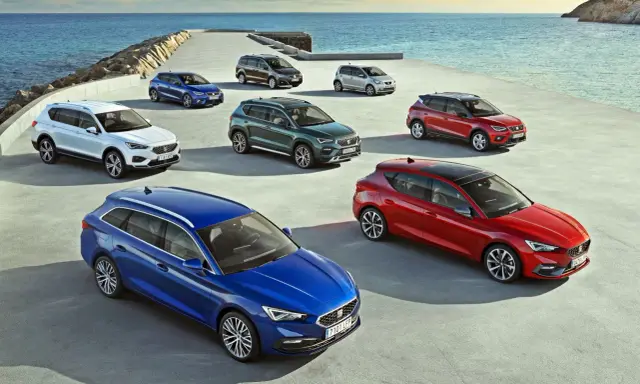 Różnorodne modele SEAT stojące nad morzem. Wśród nich biały SUV, niebieski kombi i czerwony hatchback.