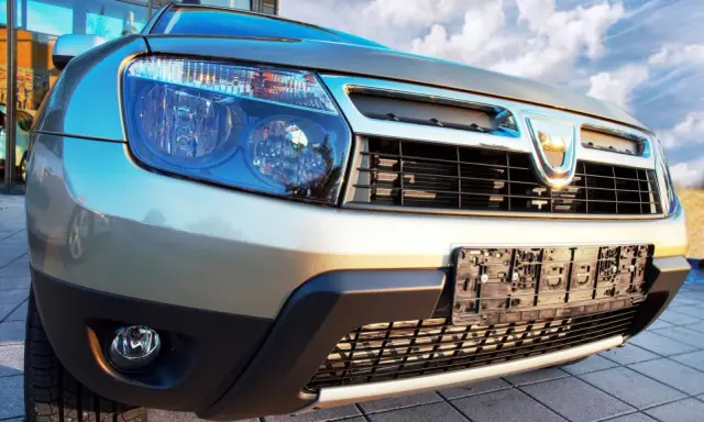 Złoty Dacia Duster 1.6 benzyna z bliska, z widocznym grillem, reflektorami i tablicą rejestracyjną.