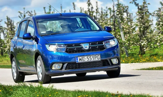 Niebieska Dacia Sandero 2025 jedzie przez kwitnący sad.