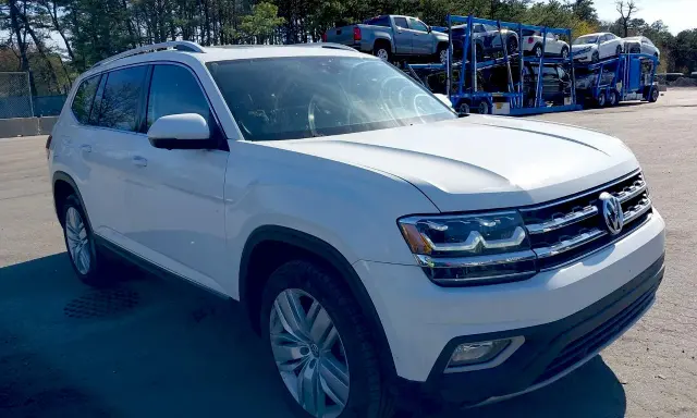 Biały VW Atlas stoi na parkingu, w tle widać lawetę z innymi samochodami.