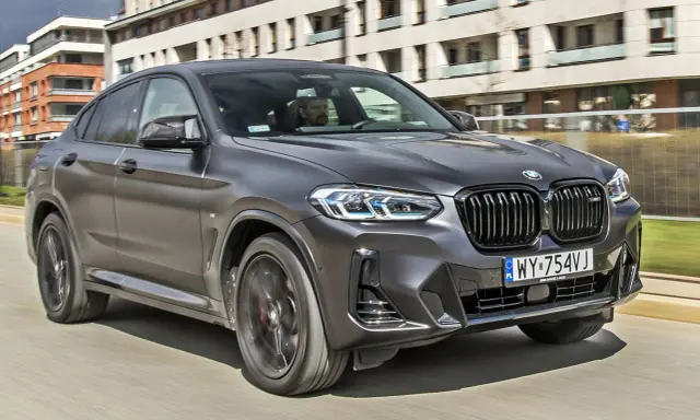 Nowy BMW X4 2025 w ciemnoszarym kolorze pędzi ulicą, z nowoczesnymi budynkami w tle.