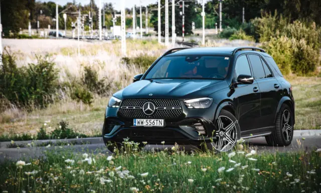 Czarny Mercedes GLE 350 z czerwonym wnętrzem zaparkowany na tle łąki i torów kolejowych.