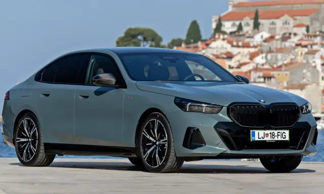 Szary BMW 520 z czarnymi felgami stoi na tle malowniczego nadmorskiego miasteczka.