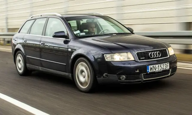 Ciemnogranatowe Audi B6 Avant pędzi autostradą. Kierowca skupiony na drodze.