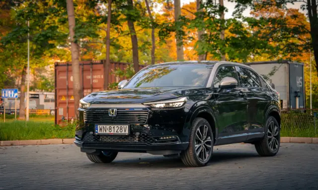Elegancki, czarny Honda HR-V 2025 na tle jesiennych drzew i kontenerów.
