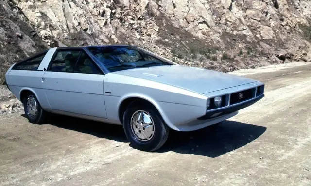 Srebrny Hyundai Pony z lat 70. na drodze w skalistym terenie.