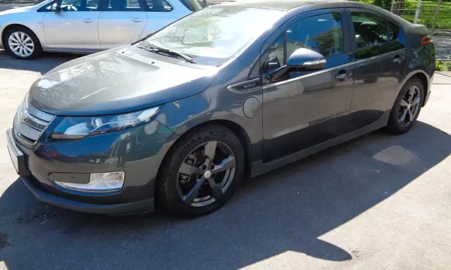 Ciemnoszary Chevrolet Volt stoi na parkingu. Obok niego widać srebrne kombi.