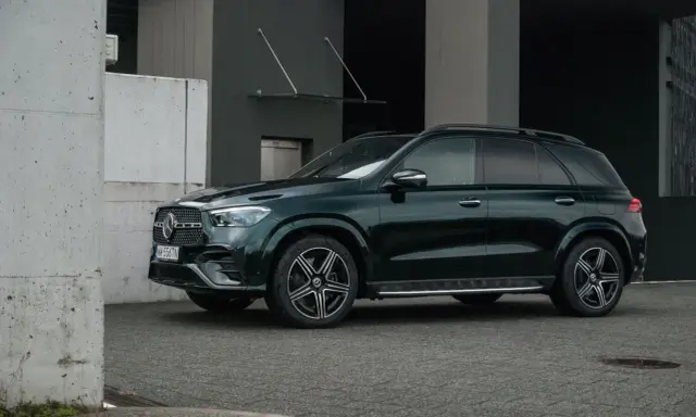 Ciemnozielony Mercedes GLE AMG stoi przed nowoczesnym budynkiem.