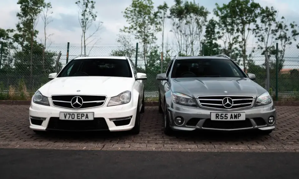 Dwa Mercedesy C63 AMG W204, biały i szary, stoją obok siebie na parkingu.
