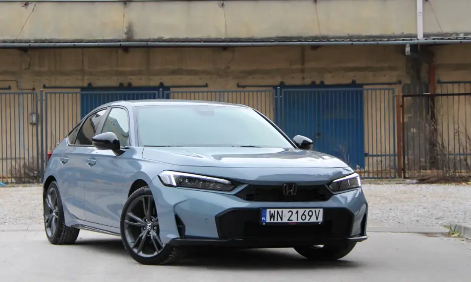 Nowy Honda Civic 11. generacji w szarym kolorze prezentuje się elegancko na tle industrialnego krajobrazu.