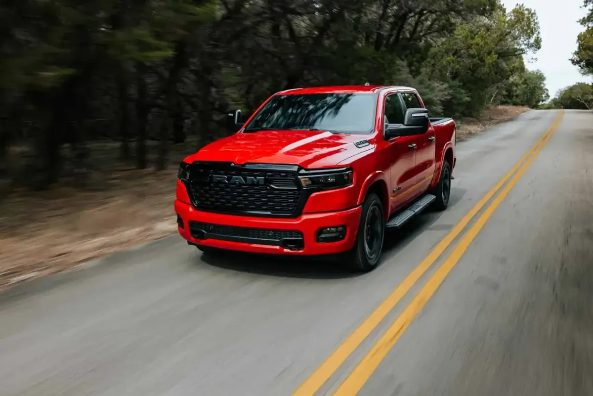 Czerwony Dodge Ram 1500 5.7 Hemi pędzi po krętej drodze wśród drzew.