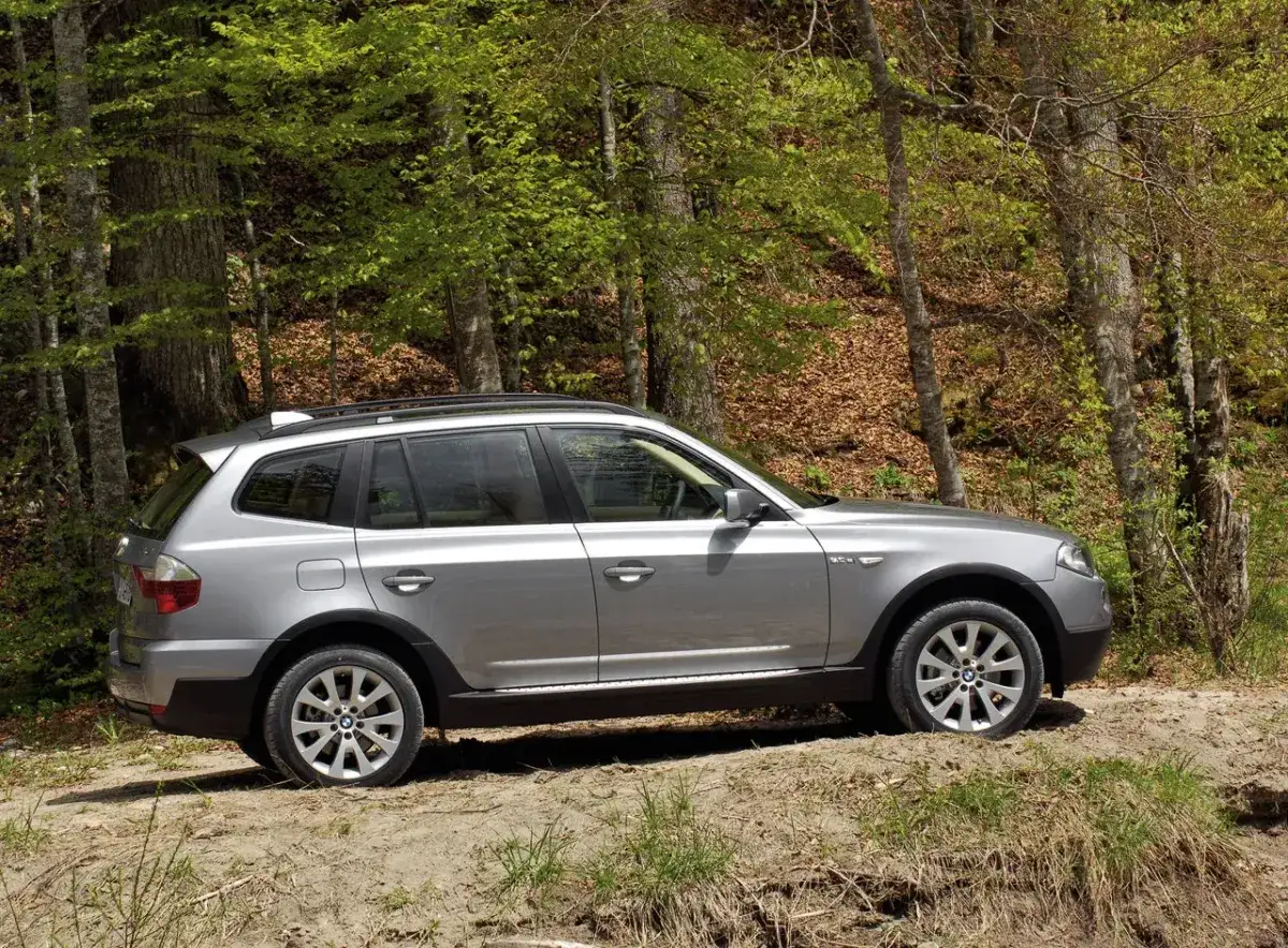 Srebrne BMW X3 E83 na leśnej ścieżce, gotowe na przygodę wśród drzew.