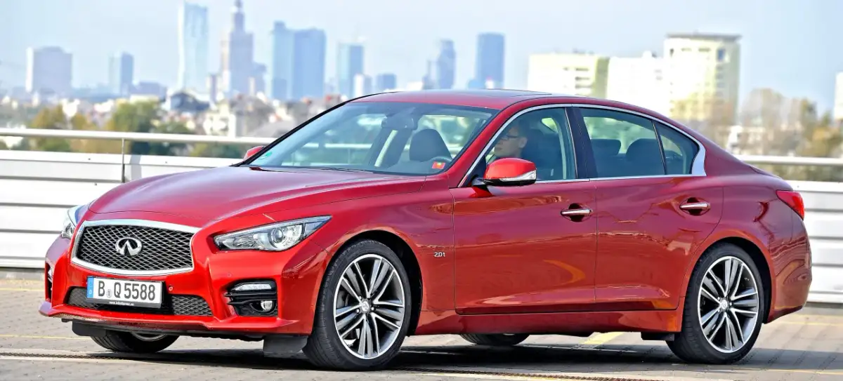 Czerwone infiniti auto z kierowcą na tle miejskiej panoramy.