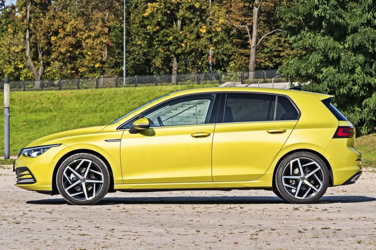 Żółty hatchback z przyciemnianymi szybami stoi na tle zieleni i drzew.