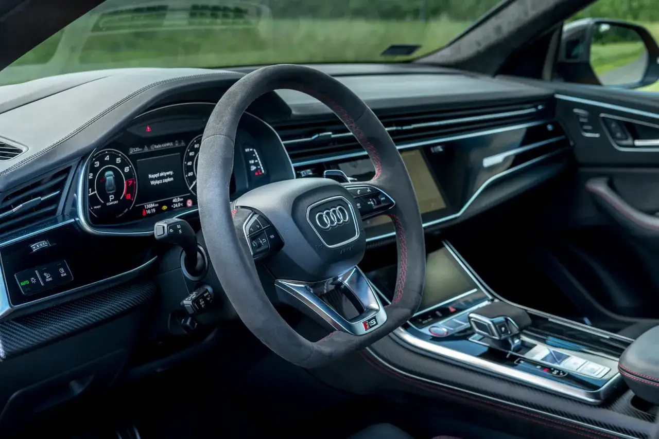 Wnętrze Audi RS Q8 z kierownicą obszytą alcantarą i czerwonymi przeszyciami. Cyfrowy kokpit i elegancka konsola środkowa.