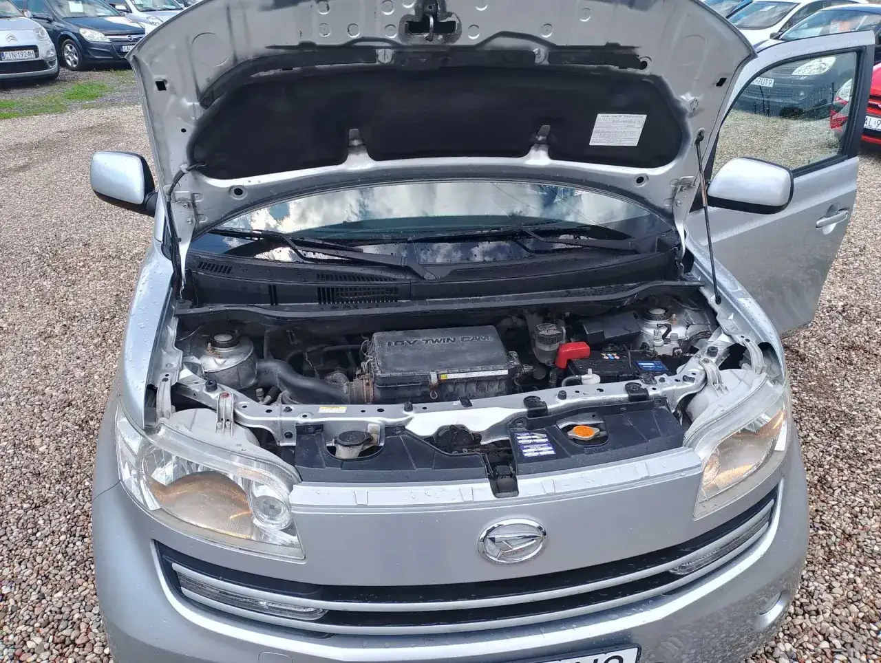 Srebrny Daihatsu Materia z otwartą maską, widoczny silnik i przednia część samochodu.