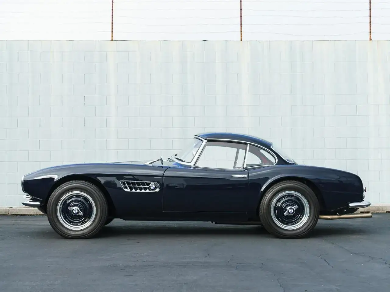 Elegancki, granatowy BMW 507 z lat 50. prezentuje swoje klasyczne linie na tle białej, ceglanej ściany.