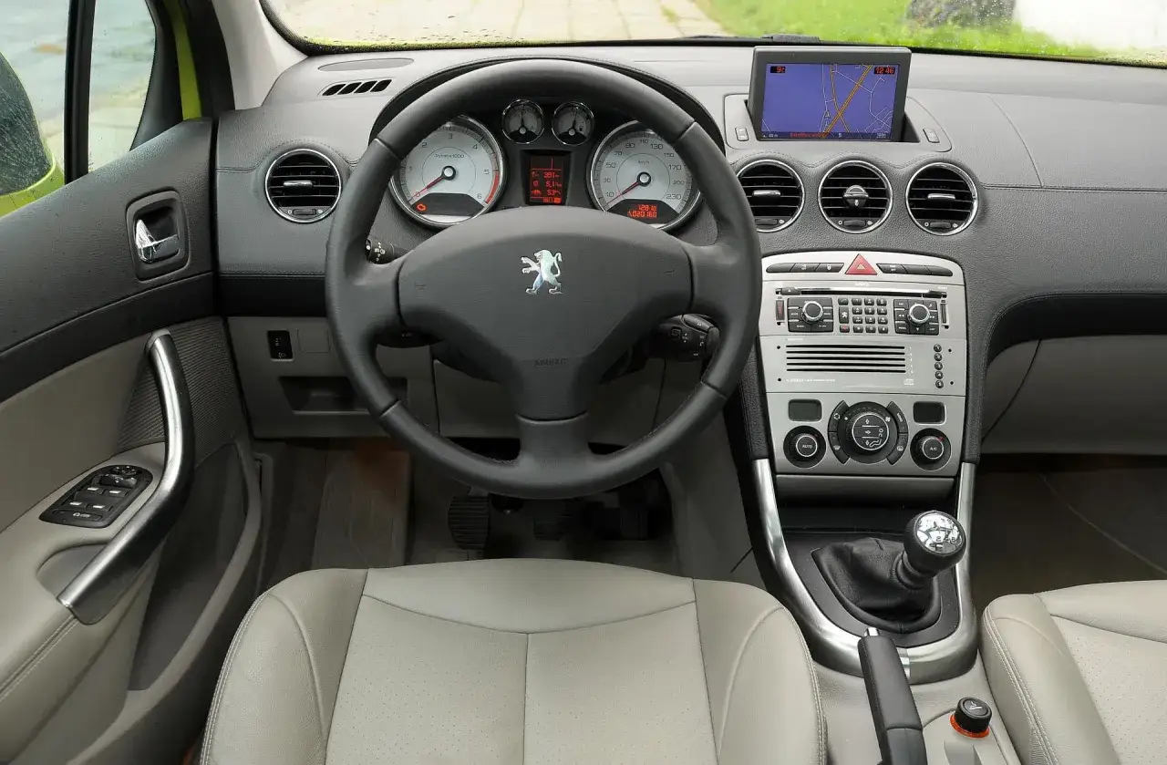 Wnętrze Peugeota 308: kierownica, deska rozdzielcza z nawigacją i panel sterowania. Jasna, perforowana tapicerka fotela.