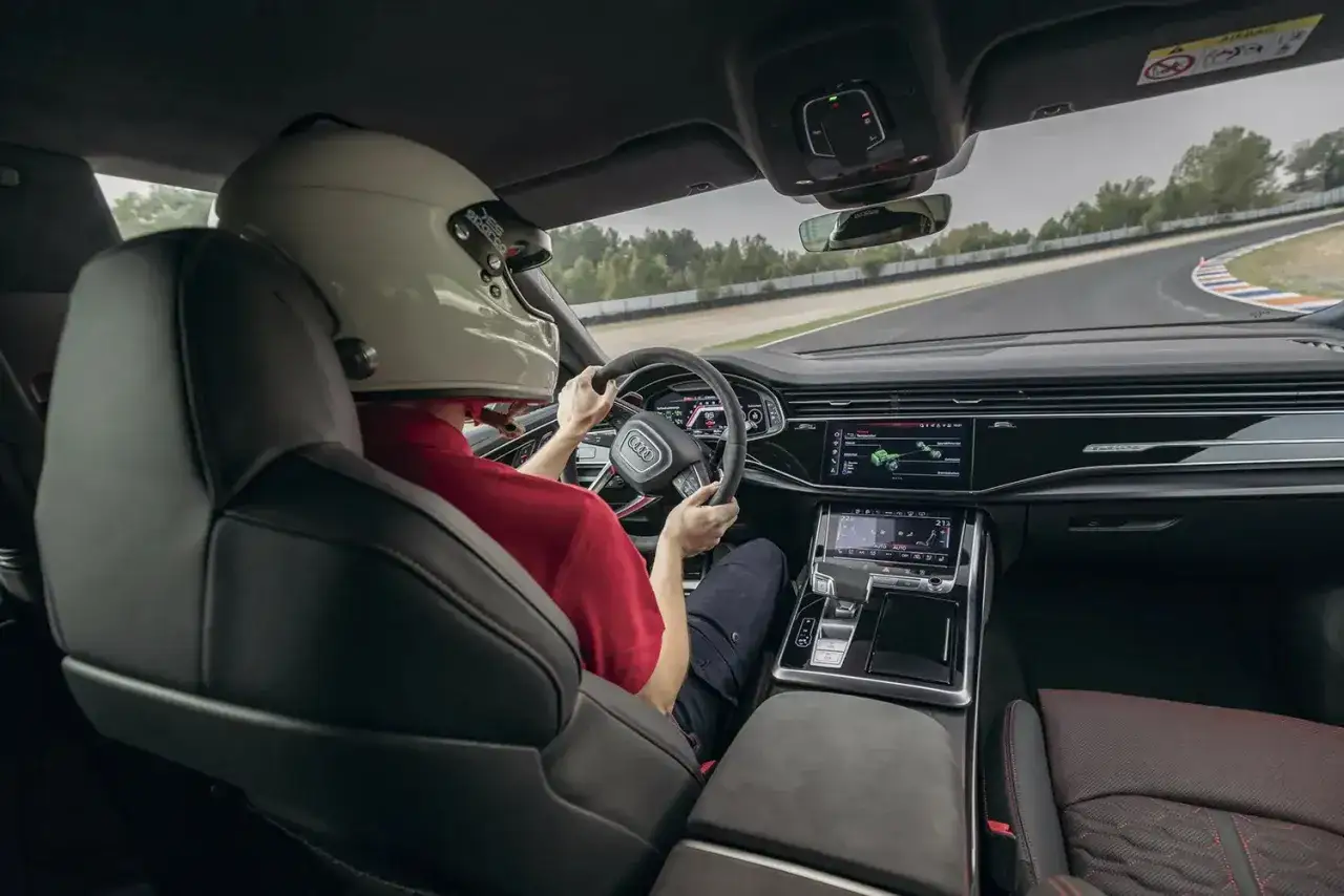 Kierowca w kasku za kierownicą Audi RS Q8 na torze wyścigowym.