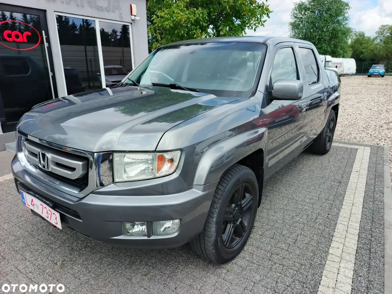 Szary Honda Ridgeline na parkingu przed salonem samochodowym.