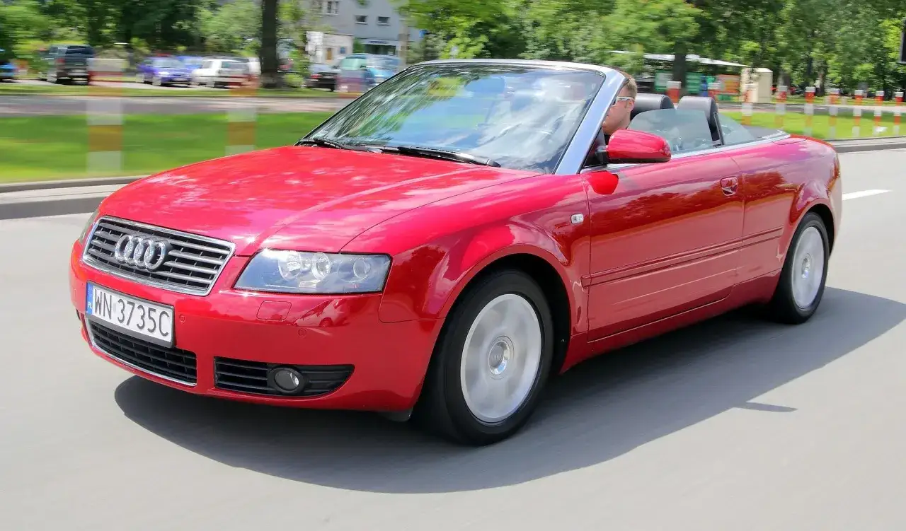 Czerwony kabriolet Audi B6 z otwartym dachem jedzie po drodze.