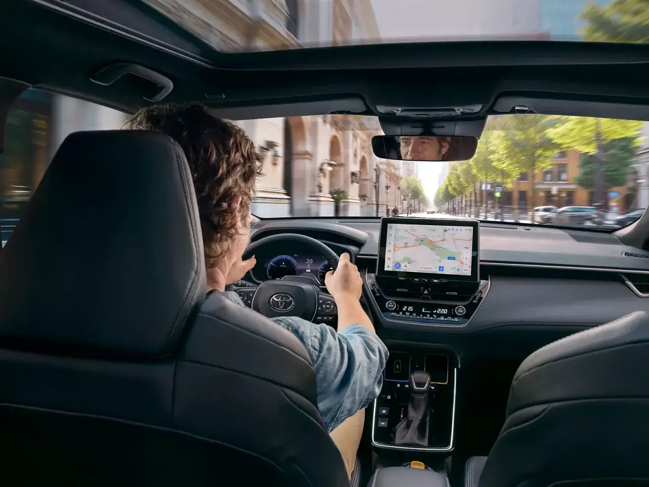 Wnętrze Toyoty Corolla 2.0 Hybrid. Kierowca zapatrzony w nawigację na ekranie centralnym, podczas jazdy miejskiej.