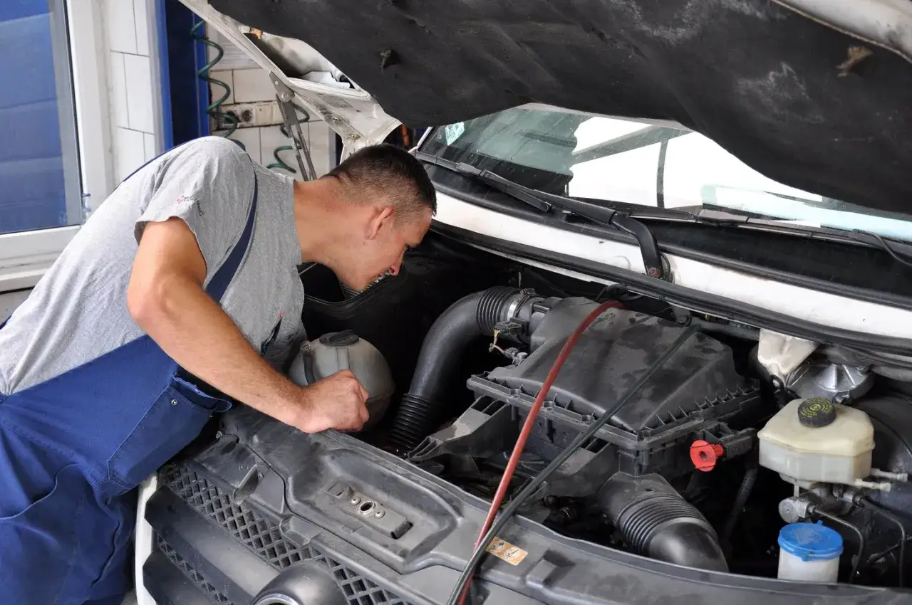 Mechanik w niebieskim ogrodniczkach pochyla się nad silnikiem, przygotowując się do wymiany uszczelki pod głowicą.