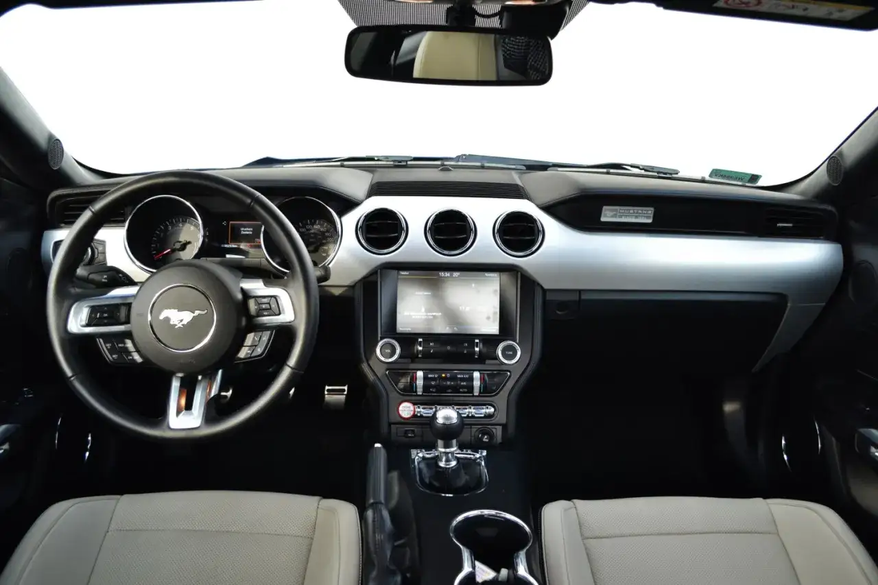 Wnętrze Ford Mustang 2.3 Ecoboost: kierownica z logo konia, ekran multimedialny, dźwignia zmiany biegów i jasne fotele.