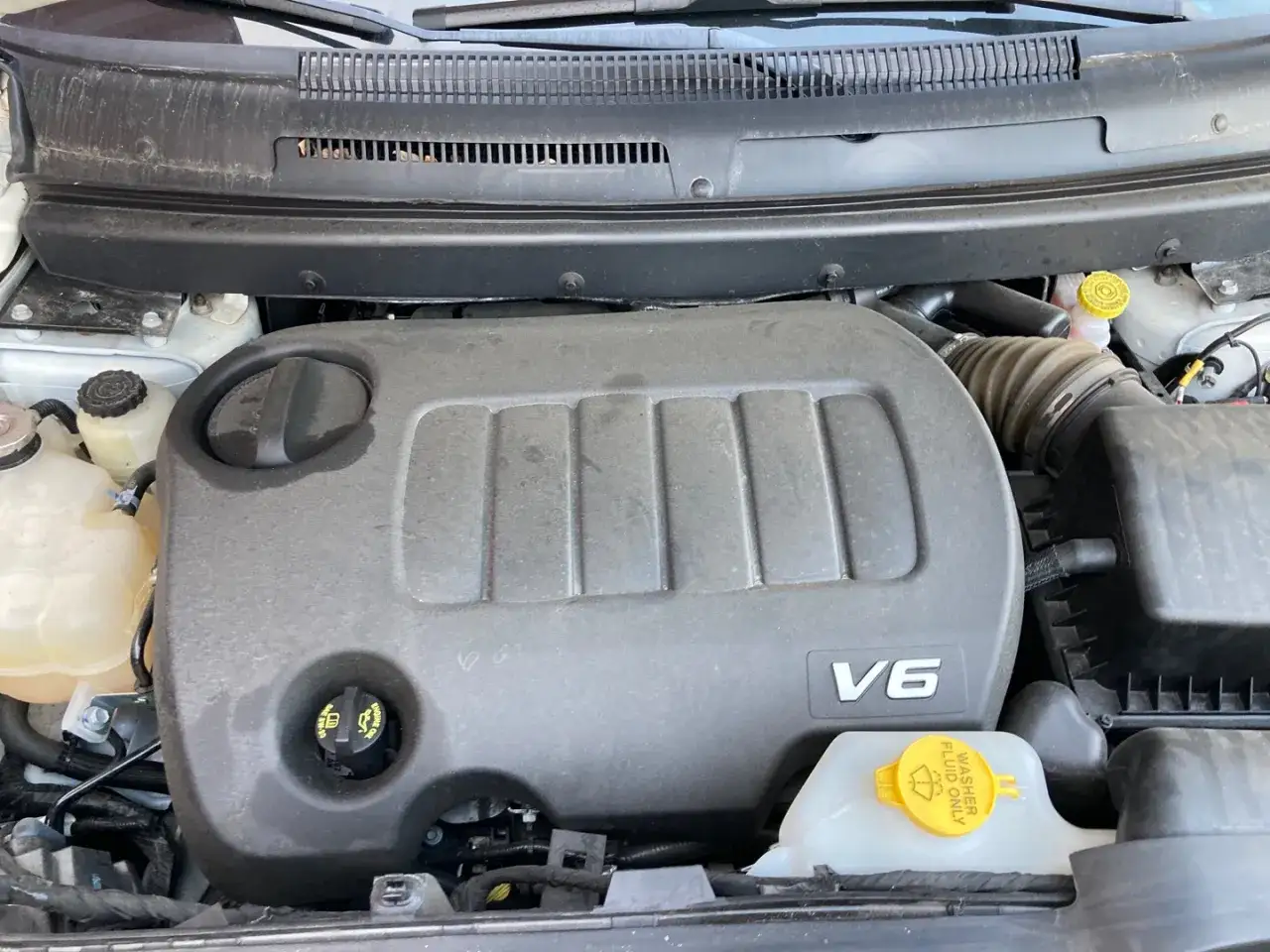 Silnik V6 w Dodge Journey 3.6. Widoczny jest plastikowy wlot powietrza i zbiornik płynu do spryskiwaczy.