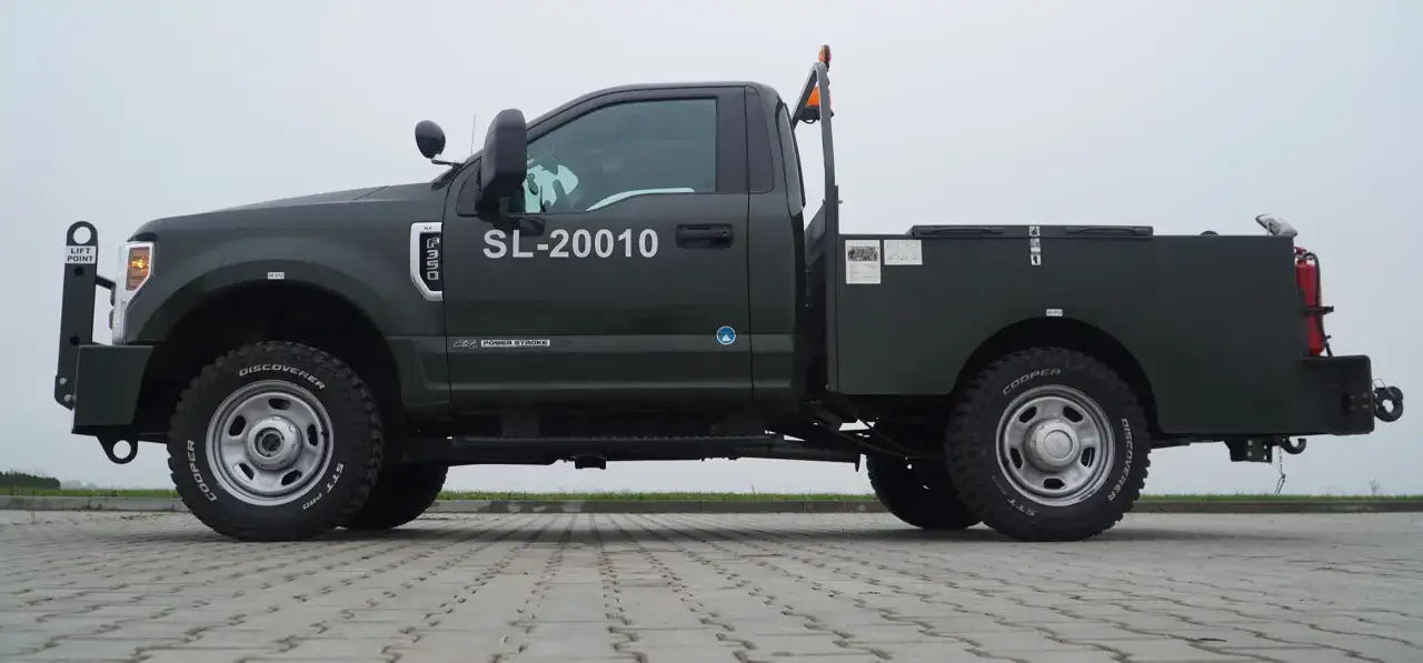 Ciemnozielony Ford F350 z numerem SL-20010, wyposażony w terenowe opony Cooper Discoverer STT Pro, gotowy do pracy.
