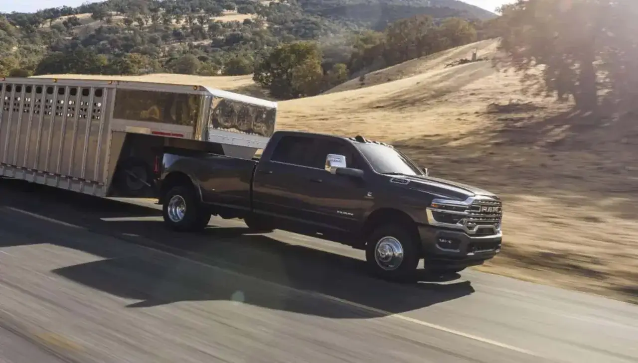 Ciemny Dodge Ram 3500 z przyczepą transportową jedzie po drodze w słoneczny dzień.
