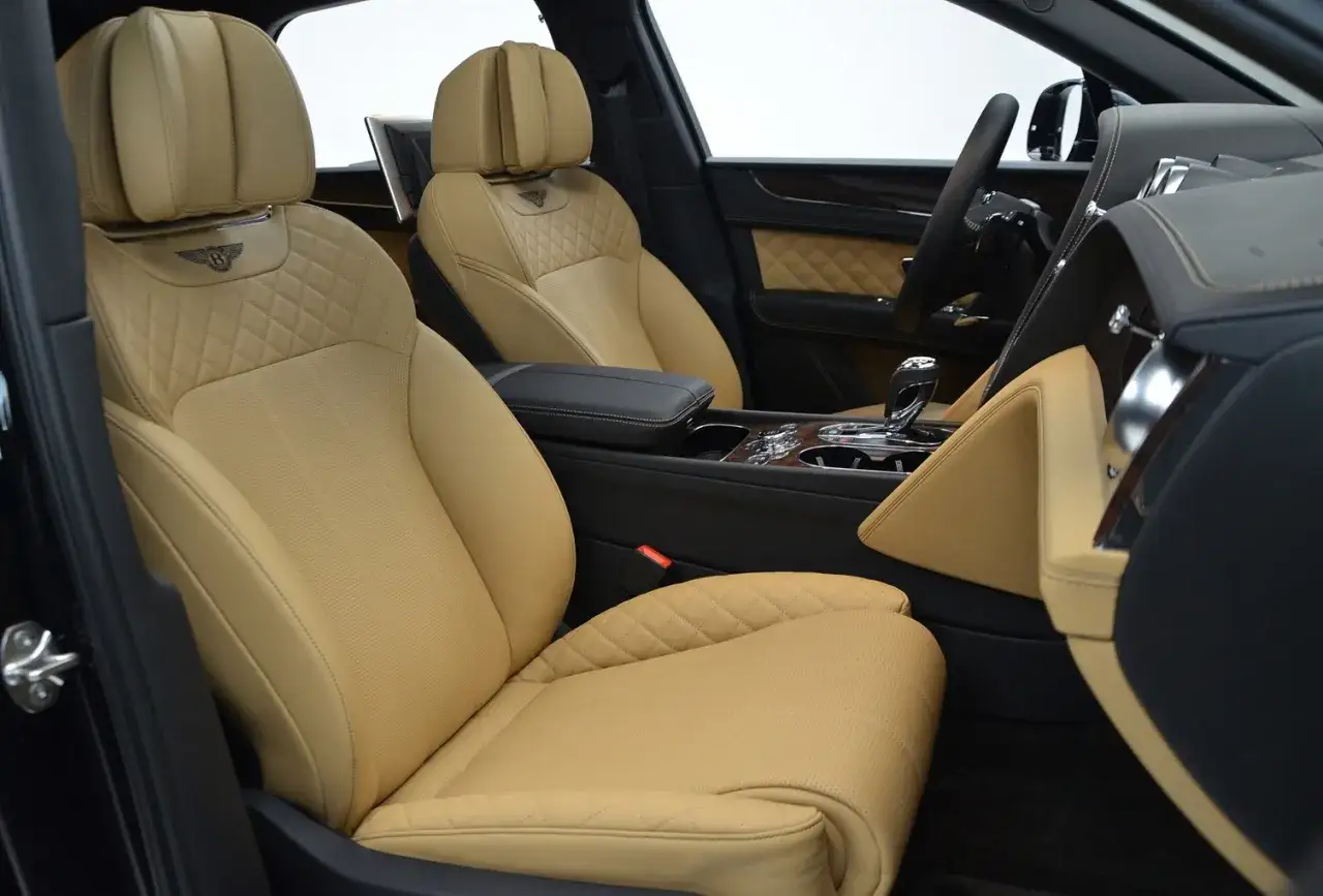 Wnętrze luksusowego Bentley'a SUV, z beżowymi skórzanymi fotelami z pikowanymi detalami i logo marki.
