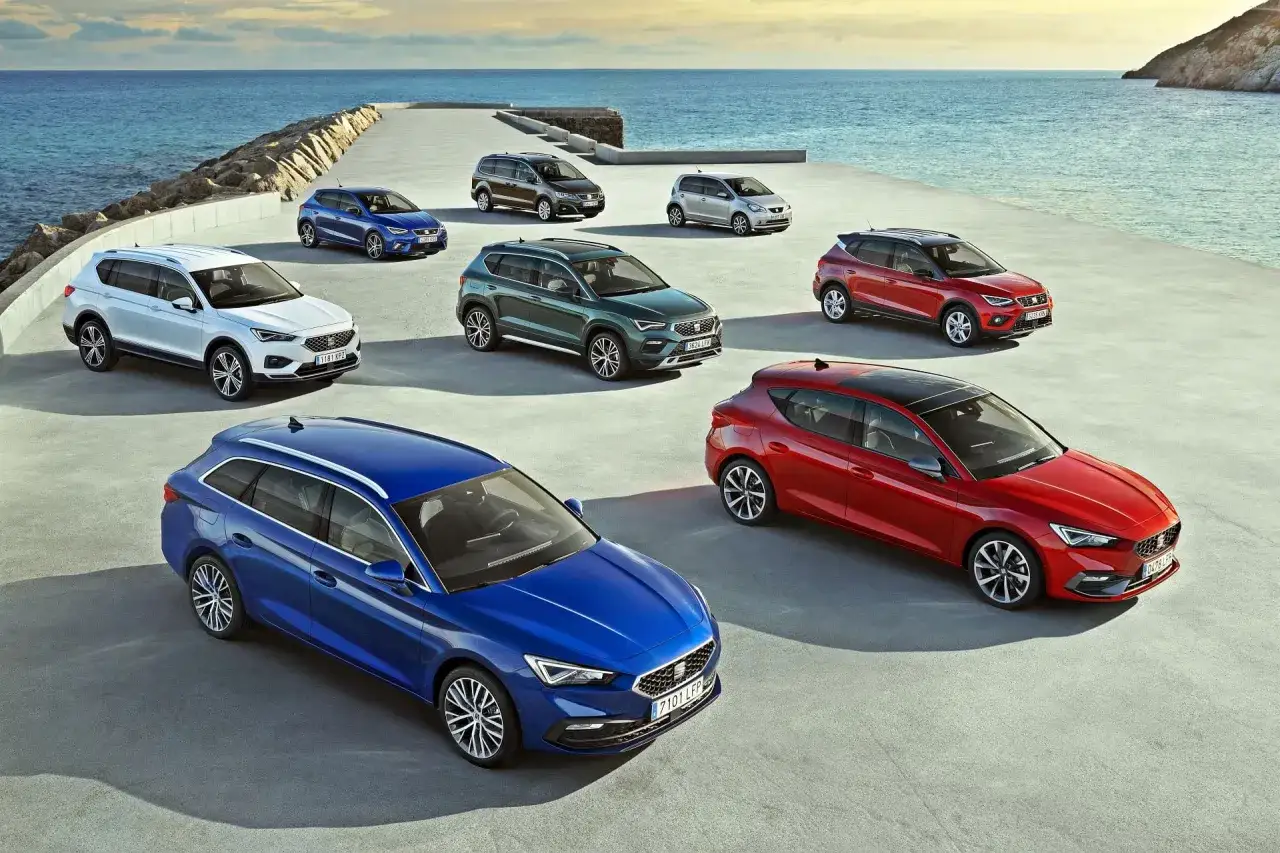 Różnorodne modele SEAT stojące nad morzem. Wśród nich biały SUV, niebieski kombi i czerwony hatchback.