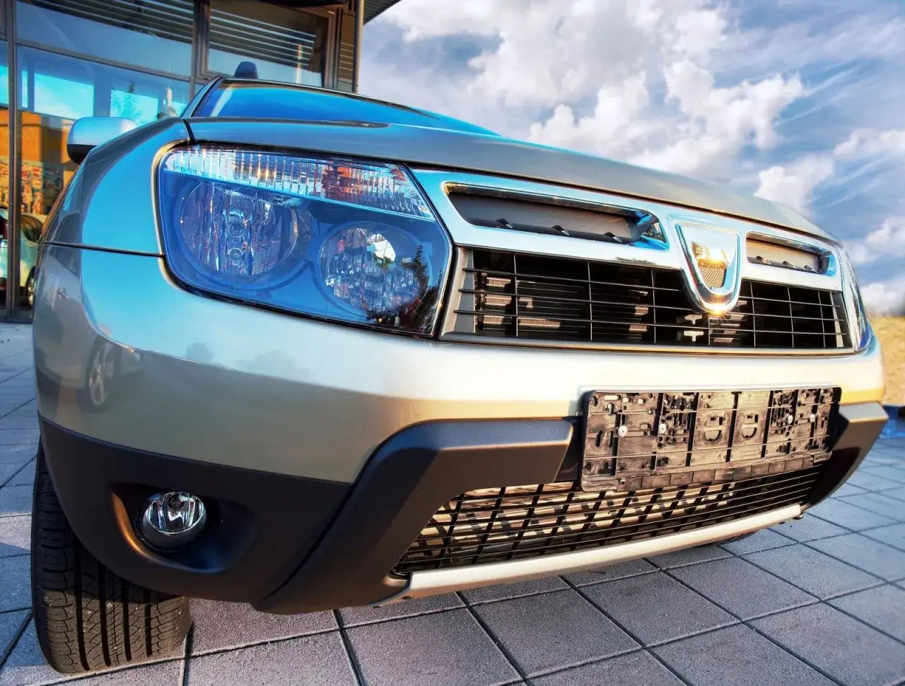 Złoty Dacia Duster 1.6 benzyna z bliska, z widocznym grillem i reflektorami.