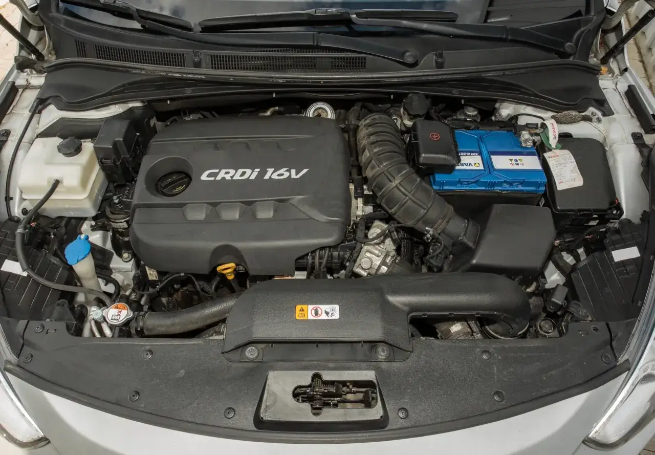 Silnik Kia Sportage 1.7 CRDi. Widoczny czarny plastikowy kolektor, niebieski akumulator i inne elementy komory silnika.