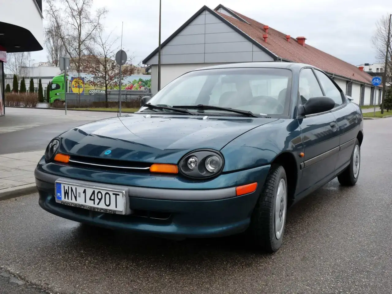 Zielony Dodge Neon z tablicą rejestracyjną WN 1490T stoi na mokrej drodze.