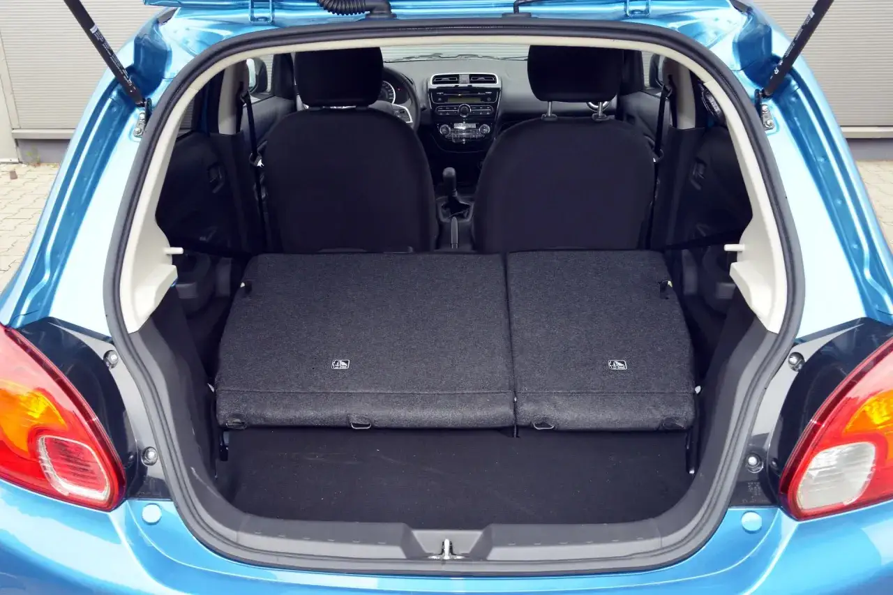 Błękitny Mitsubishi Space Star z otwartym bagażnikiem. Widoczne złożone tylne siedzenia, tworzące płaską przestrzeń bagażową.