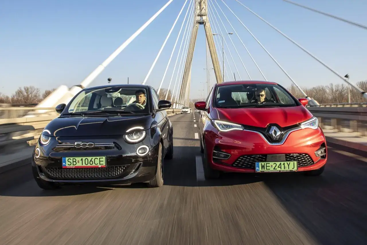 Czarny fiat elektryczny i czerwony samochód jadą obok siebie po moście.