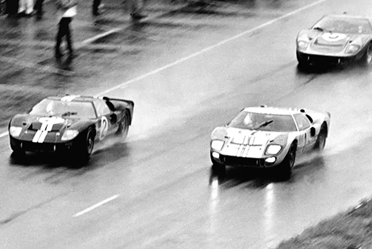 Trzy samochody Ford GT40 ścigają się po mokrym torze.