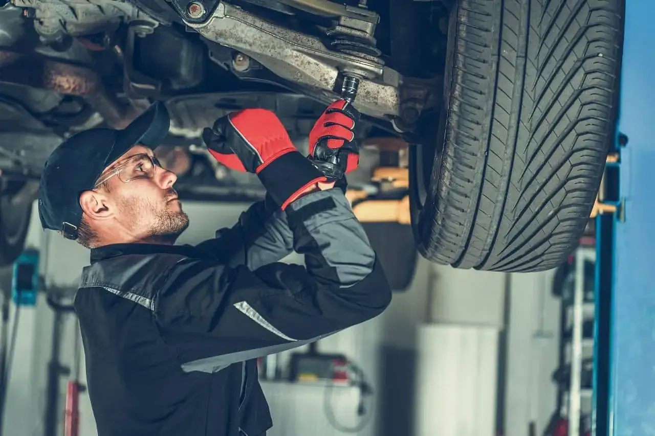 Mechanik dokręca sworznie wahaczy, pracując pod podniesionym samochodem.