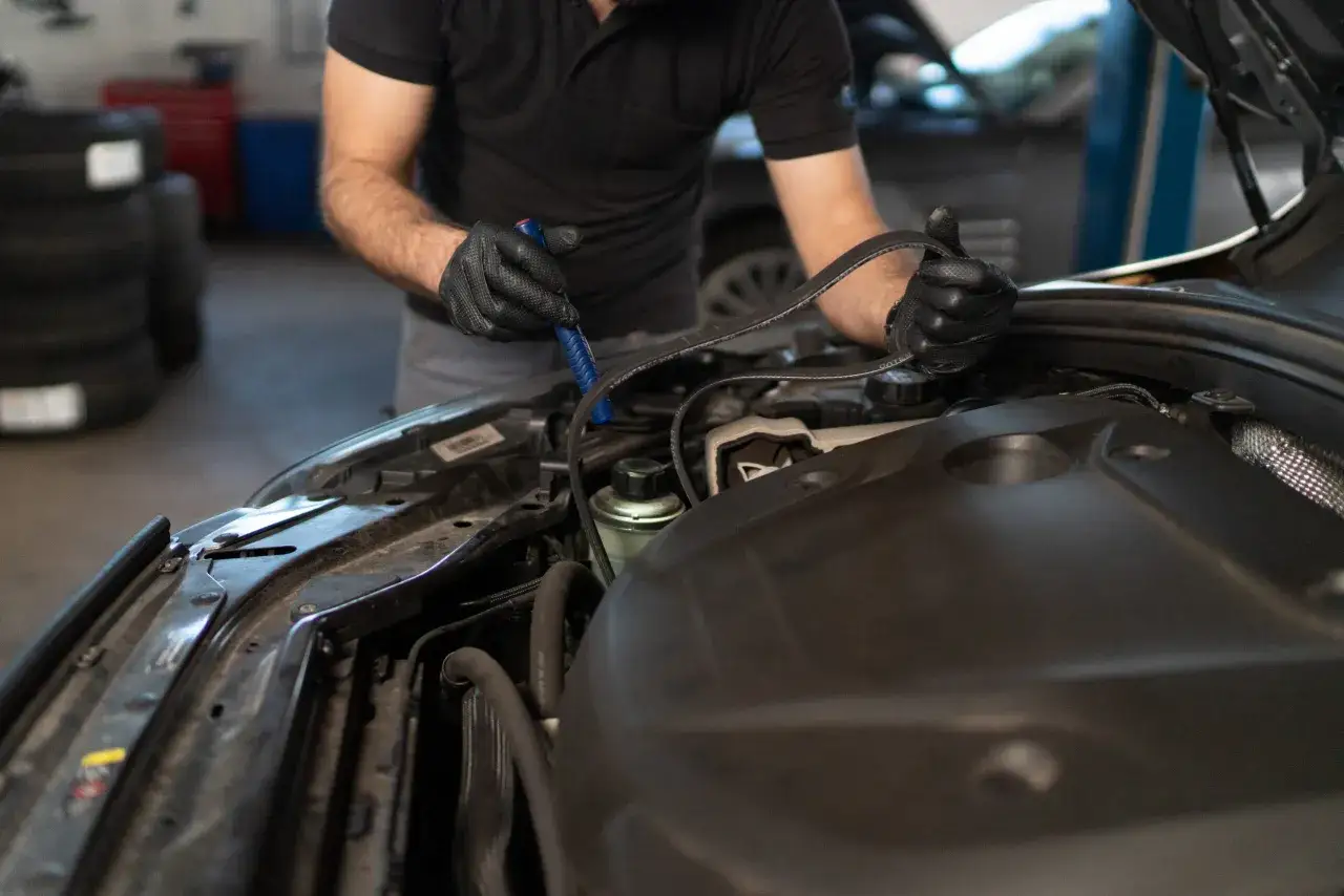 Mechanik w czarnej rękawiczce trzyma nowy pasek, przygotowując się do wymiany paska rozrządu w silniku samochodu.