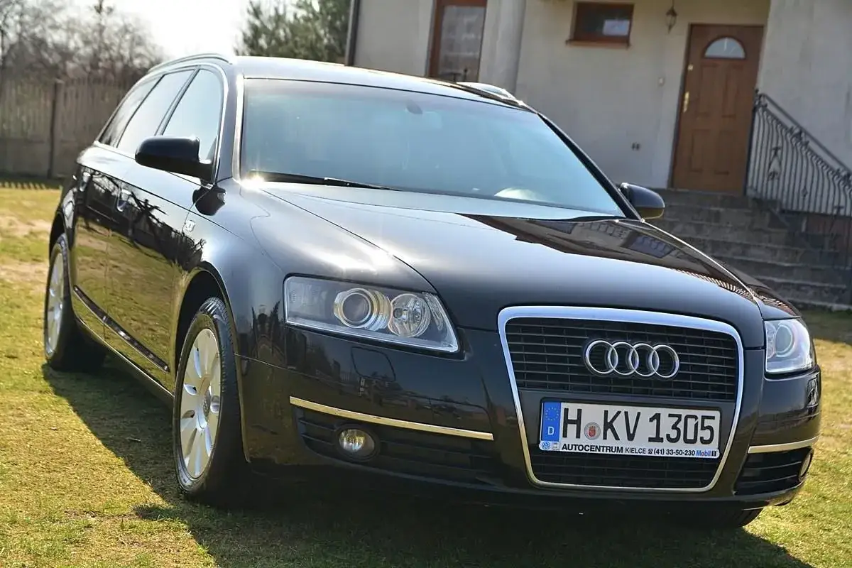 Czarny Audi C6 Avant lśni na trawie przed domem. Elegancki kombi z charakterystycznym grillem i światłami.