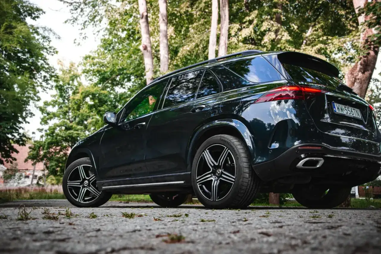 Ciemny Mercedes GLE 350 zaparkowany na kamienistej drodze, otoczony zielenią drzew.