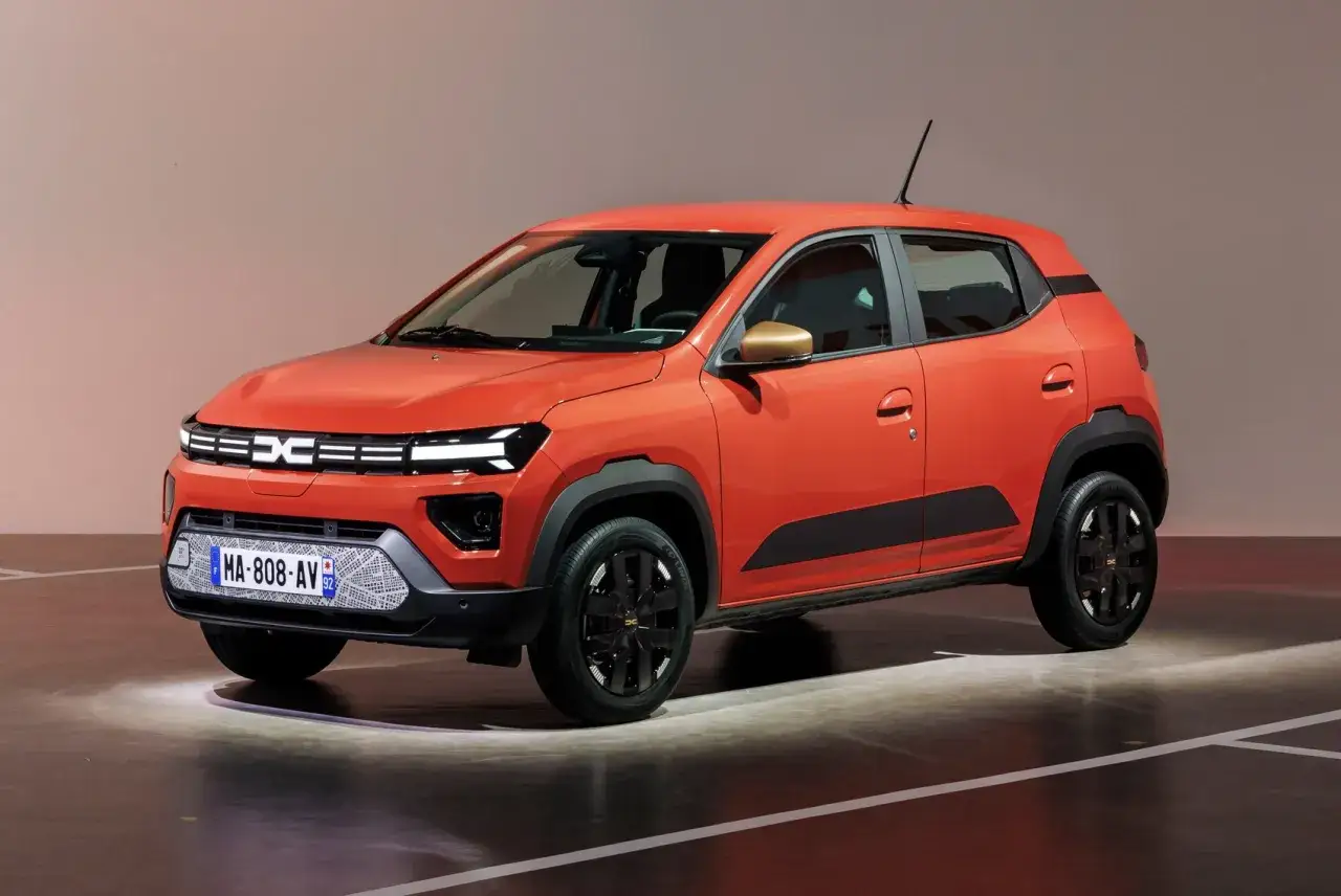 Pomarańczowy dacia elektryk z czarnymi akcentami i złotymi lusterkami stoi na scenie.